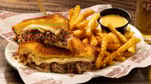 Plate of short rib grilled cheese sandwich with french fries and cheese dip.