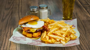 Plate serving a breakfast burger with eggs over easy and a side of French fries.