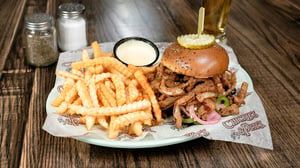 A plate with a pulled port sandwich with fried and pickled onions and a side of french fries.