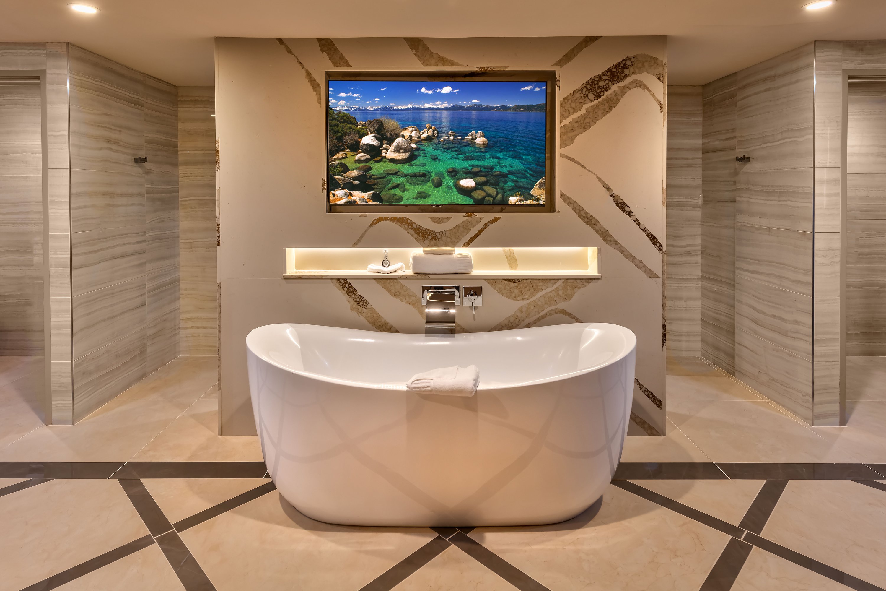 A freestanding tub in a marble-lined bathroom with a large artwork above it.