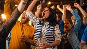 Photo of fans standing in bar cheering for sports team.